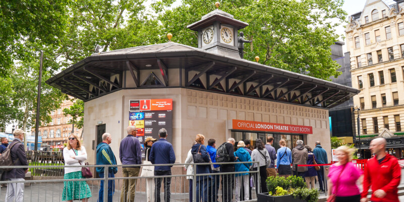People queue outside the Official London Theatre ticket booth in Leicester Square on a summer day.